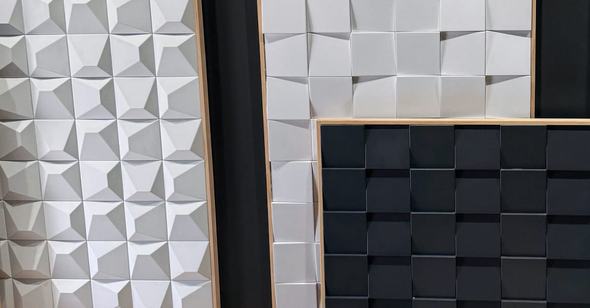 Panneaux en relief composés de formes géométriques, deux panneaux blancs avec des motifs en relief et un panneau noir avec une texture carrée.