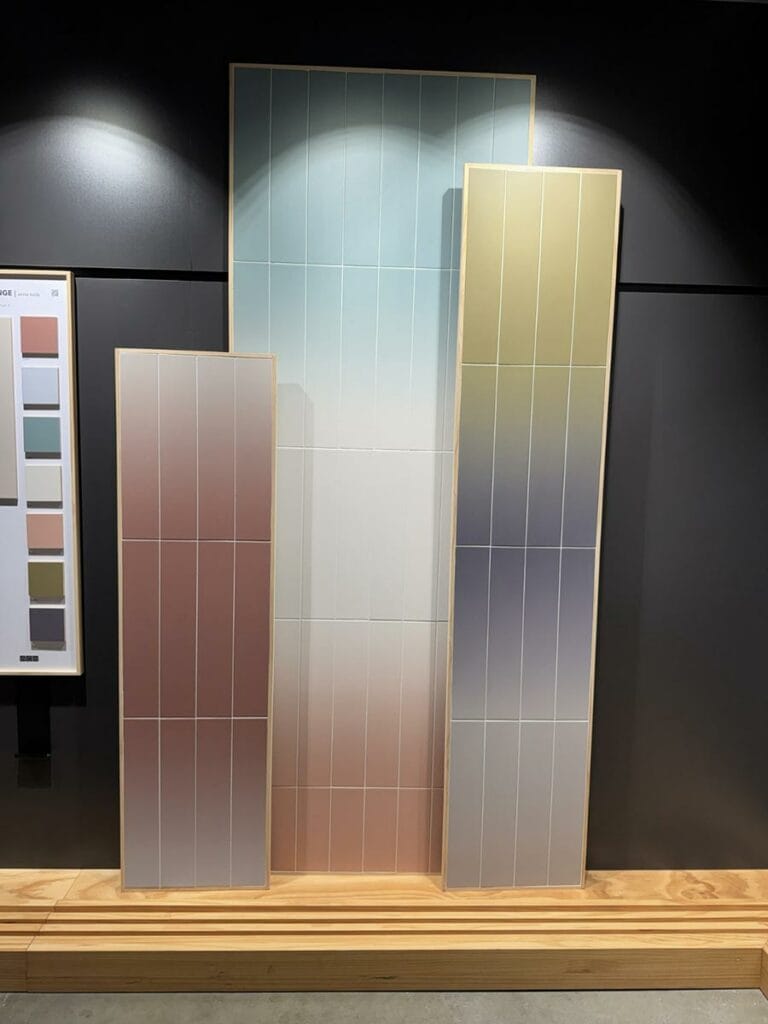 Trois panneaux verticaux de couleur avec un dégradé, disposés sur une base en bois. Le panneau de gauche est rose, le panneau du milieu est bleu clair, et le panneau de droite est beige.