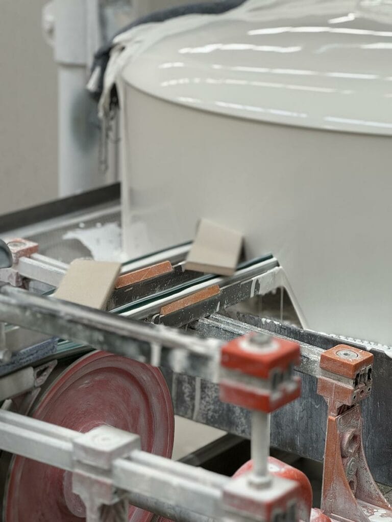 Machine tool with a circular saw cutting a glossy white object, with orange clamps and metal guide rails visible.