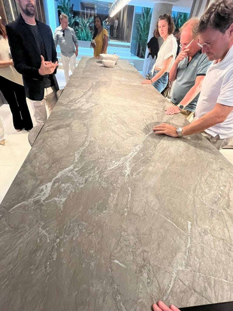 Table en marbre gris avec des veines blanches, entourée de plusieurs personnes discutant et touchant la surface.