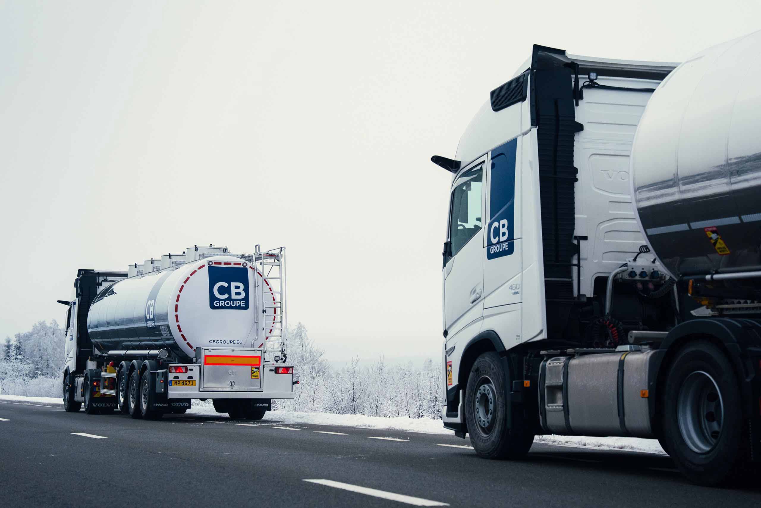 Deux camions-citernes CB Group roulant sur une route enneigée.